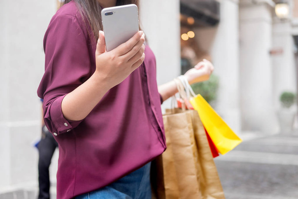 Woman look at mobile phone with paperbags in the mall while enjoying a day shopping - Photo, Image