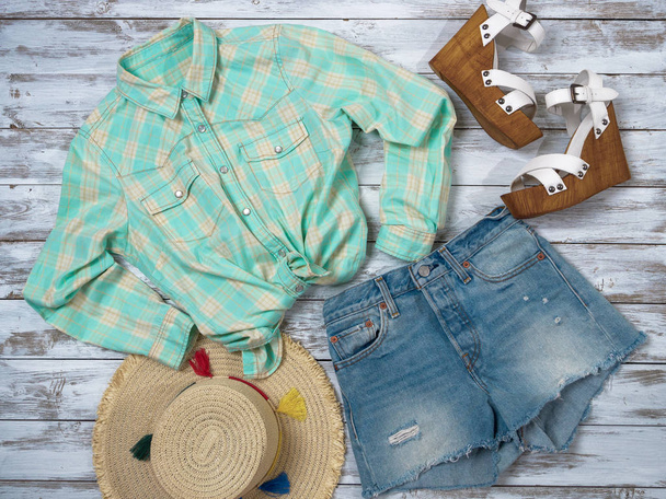 Womens clothing, accessories, shoes (plaid shirt, denim shorts, straw hat, wedge sandals). Fashion outfit, spring summer collection. Shopping concept. Flat lay, top down view - Photo, Image