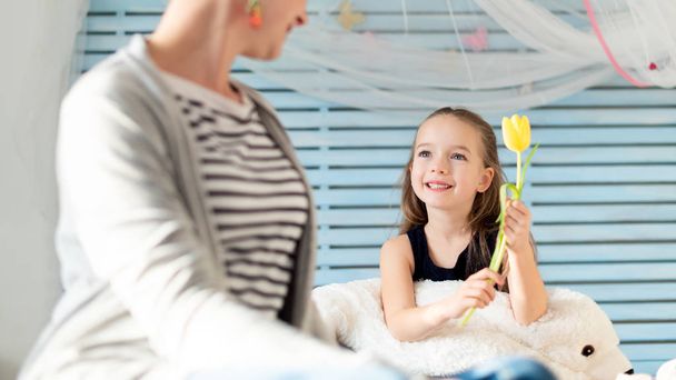 Cute young girl giving her mom a flower. Family celebration concept. Happy Mother's Day or Birthday Background.  - Fotó, kép