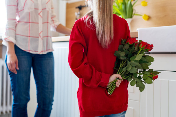 Happy Mother's Day or Birthday Background. Adorable young girl surprising her mom with bouquet of red roses. Family celebration concept. - Foto, immagini