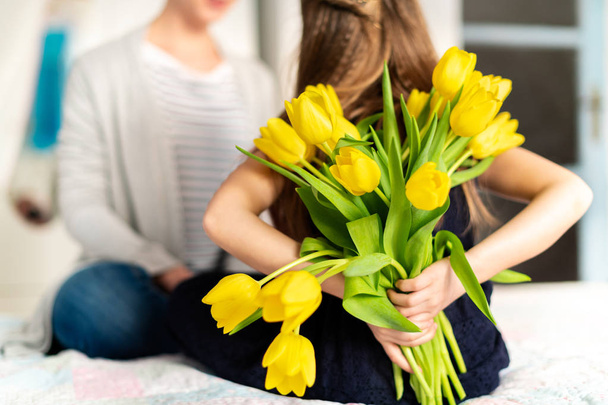 Happy Mother's Day or Birthday Background. Unrecognizable young girl surprising her mom with bouquet of yellow tulips. Family celebration concept. - Foto, Bild