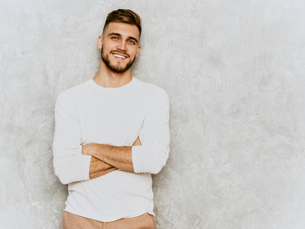 Muotokuva komea hymyilevä hipster tukkiseksuaalinen liikemies malli yllään rento kesä valkoiset vaatteet. Muoti tyylikäs mies poseeraa harmaa seinä
 - Valokuva, kuva