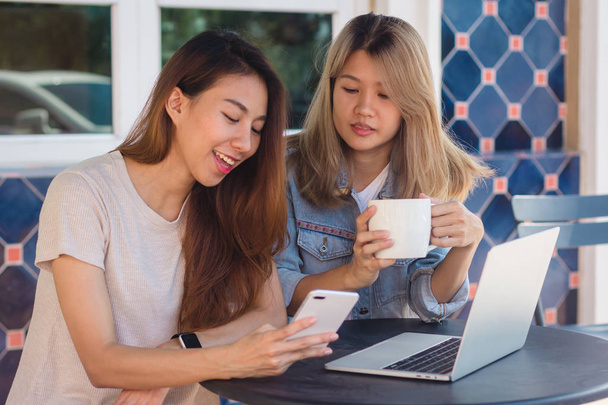 Asian young women working on laptop using and looking smartphone and drinking coffee while sitting in cafe. Lifestyle women communication and working in coffee shop concept. - Photo, Image