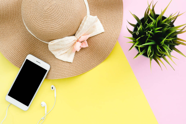 Плаский дизайн подорожі в літній концепції - вид зверху на літній капелюх, смішний смартфон, навушники та маленьке дерево на рожево-жовтому пастельному кольоровому просторі. подорожі влітку на пастельному кольоровому фоні
. - Фото, зображення