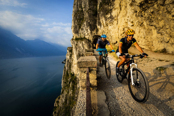 女と男の日の出山とガルダ湖の景色でバイクに乗ってサイクリング。Mtb エンデューロ流れ sentiero ponale トレイルをサイクリング カップルを追跡します。アウトドア スポーツ活動. - 写真・画像
