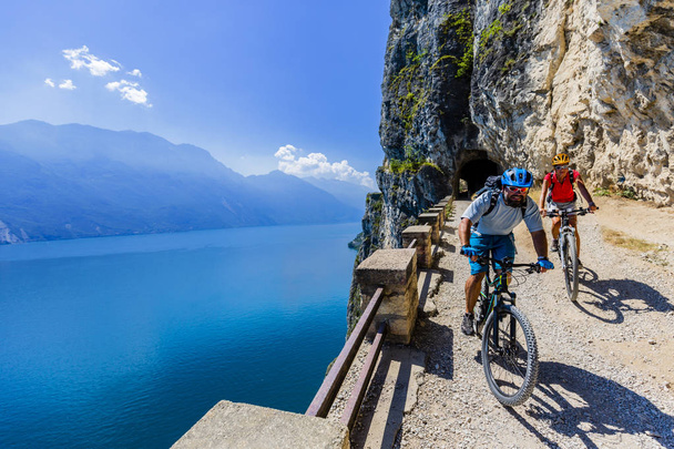 Pyöräily nainen ja mies ratsastus polkupyörillä auringonnousun vuorilla ja Garda järvi maisema. Pari pyöräily MTB enduro virtaus sentiero ponale trail track. Ulkoilutoiminta
. - Valokuva, kuva