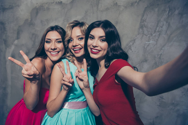 Self-portrait of three nice-looking lovely chic elegant attractive glamorous cheerful cheery ladies in maroon burgundy mint pink clothes showing v-sign over gray concrete wall - Фото, изображение