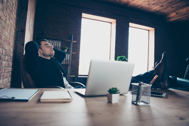 Profile side view portrait of his he handsome stylish trendy guy sitting in chair having free time legs on table sleeping nap slumber at modern industrial loft interior workplace workspace - 写真・画像