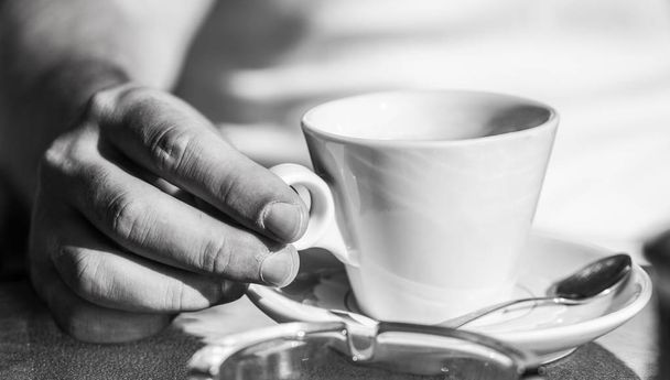 Hand van de mens houdt koffie of koffie cup op café. Kopje koffie. Cappuccino en zwarte espresso-koffie kopje. Koffie drinken. Close up van een handen van de man met een hete koffie kopjes. Zwart-wit - Foto, afbeelding