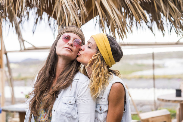 Paar junger Frauen küssen sich mit Liebe und Romantik im Freien mit Stühlen und Tischen - gleichgeschlechtliche Liebe - hippes Freiheitsstilkonzept für Menschen alternativer Lebensstil  - Foto, Bild
