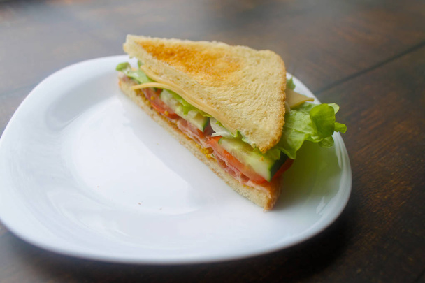 Sandwich with bacon, cheese and fresh vegetables.  Preparing a sandwich with scrambled eggs, bacon and cheese. - Photo, Image