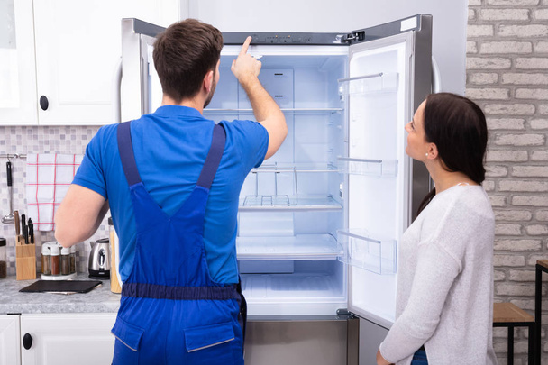 Young Woman Looking At Male Serviceman Checking Temperature Of Refrigerator - Фото, зображення