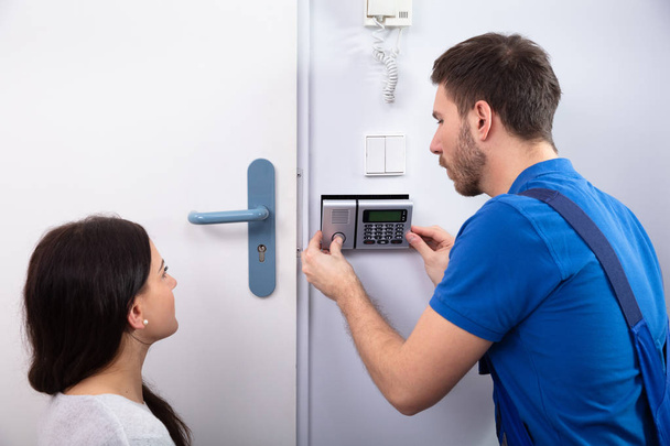 Close-up Of Handyman Installing Security System Near Door Wall While Woman Using Remote - Zdjęcie, obraz