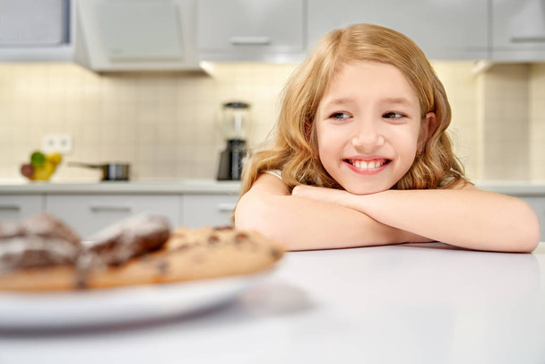 Girl leaning on table and looking at tasty cookies. - Φωτογραφία, εικόνα