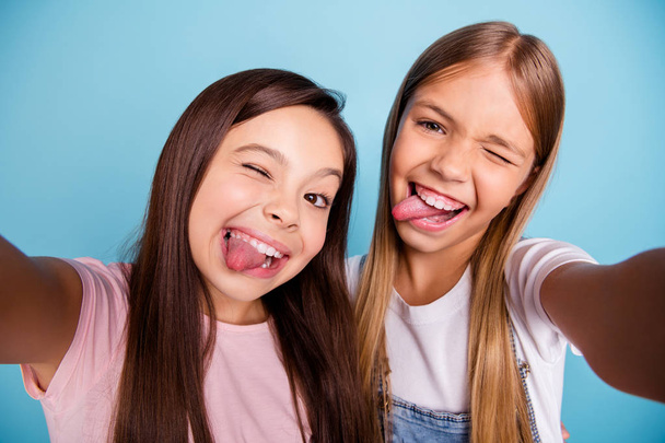 Close up photo two pretty little age girls holiday having fun funky tongue out of mouth make take selfies long pretty hair wearing casual jeans denim t-shirts isolated on blue bright background - Zdjęcie, obraz