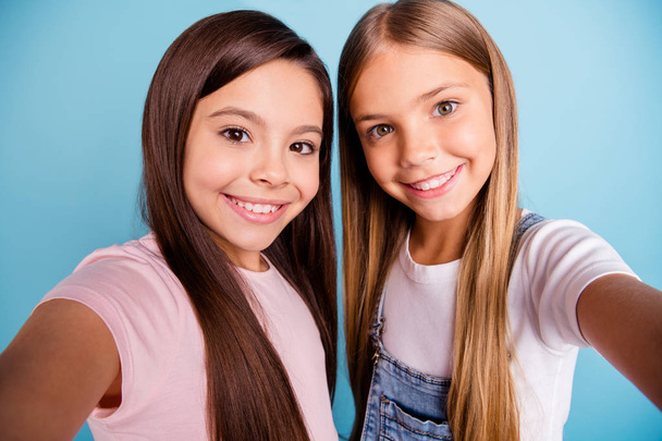 Close up photo two little she her blond brunette girls long pretty hair telephone make take selfies mom mommy skype talk tell speak wearing casual jeans denim t-shirts isolated blue bright background - Фото, зображення