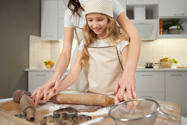 Mother helping, teaching daughter to squeeze dough. - Zdjęcie, obraz