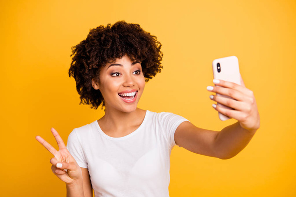 Close-up portrait of her she nice cute sweet attractive lovely cheerful glad funny wavy-haired lady holding in hands cell making selfie showing v-sign isolated on bright vivid shine yellow background - 写真・画像