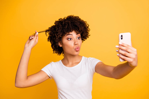 Close-up portrait of her she nice cute attractive lovely cheerful funny wavy-haired lady holding in hands cell making selfie touching playing with curl isolated on bright vivid shine yellow background - Foto, Imagen