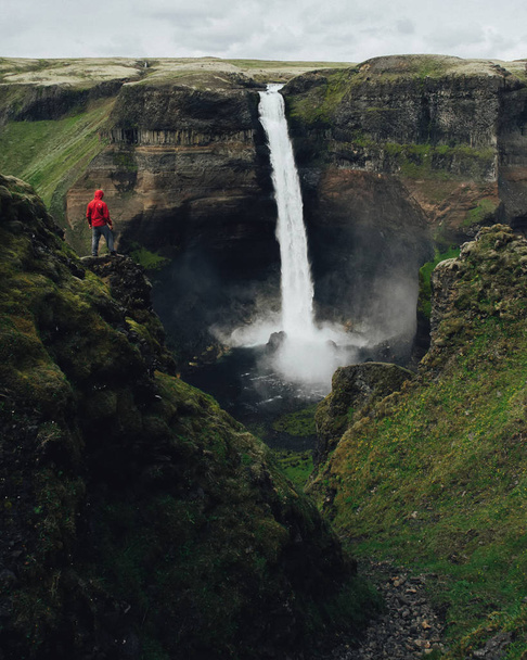 Man in red coat looking on breathtaking icelandic waterfall  - Foto, Imagem