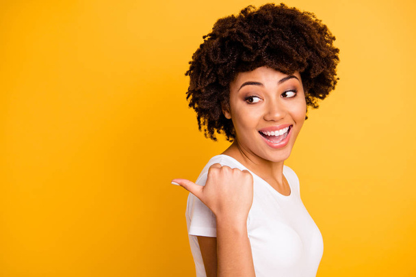 Close up photo beautiful pretty amazing she her dark skin lady arm finger point picking funny funky eyes look side laugh laughter wearing casual white t-shirt isolated yellow bright vivid background - Foto, Imagem