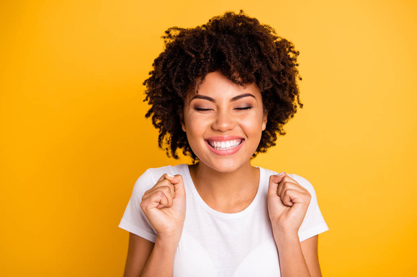 Close up photo beautiful amazing she her dark skin lady hands arms fists raised eyes closed great big win competition wear casual white t-shirt isolated yellow bright vibrant vivid background - Fotoğraf, Görsel