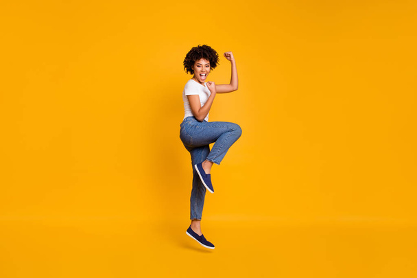 Full length body size side profile photo jumping high beautiful she her lady yelling loud voice legs fists hands arms up win wearing casual jeans denim white t-shirt clothes isolated yellow background - Fotó, kép