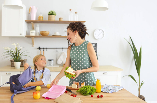 Gyönyörű barna anya és lánya, egészséges ebéd csomagolási és készül, iskola táska, a konyhában  - Fotó, kép