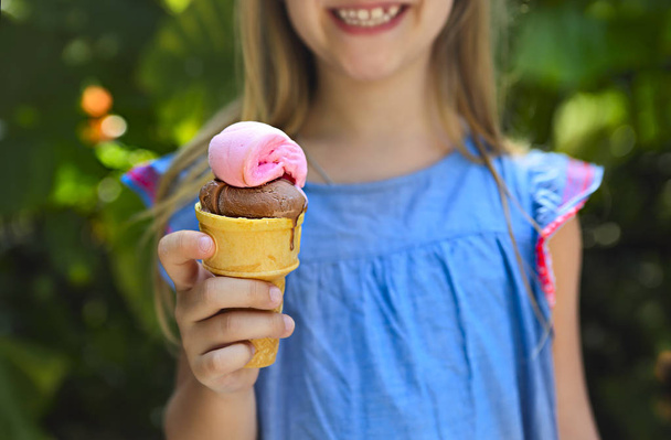 Roztomilá holčička s legrační výraz drží kužel zmrzliny mimo světlé přírodní pozadí. Blízko u - Fotografie, Obrázek