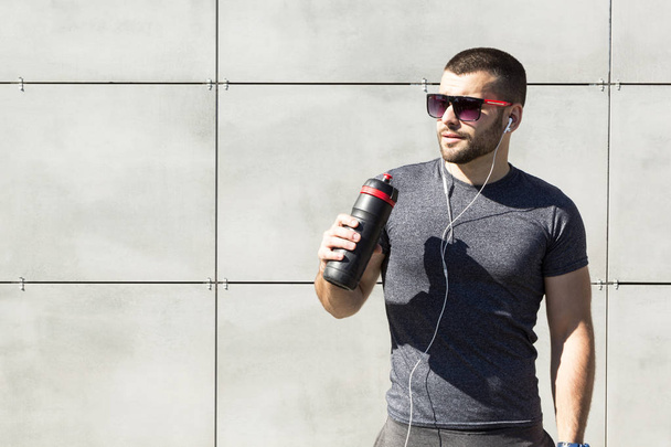A young muscular man drinks water. The concept of sport and fitness - Фото, изображение