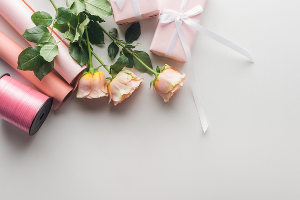 верхний вид розовых роз, рулонов бумаги и обернутых подарков с шелковой лентой на сером фоне
  - Фото, изображение