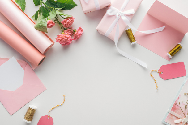 Ansicht von rosa Rosen, Papierrollen, verpackten Geschenken, Umschlag und Grußkarte auf grauem Hintergrund  - Foto, Bild