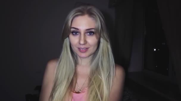 schöne junge blonde Frau mit leuchtend blauen Augen auf dunklem Hintergrund flirtet mit der Kamera, flirtet und lächelt - Filmmaterial, Video