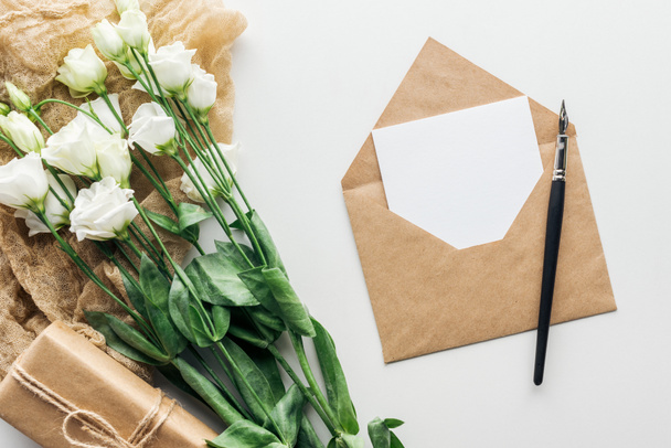 Draufsicht auf Eustoma, Umschlag mit leerer Karte, verpacktes Geschenk, Tuch und Tuschstift auf grauem Hintergrund  - Foto, Bild