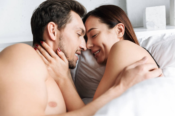 Beautiful young couple laying in bed, embracing - Fotoğraf, Görsel