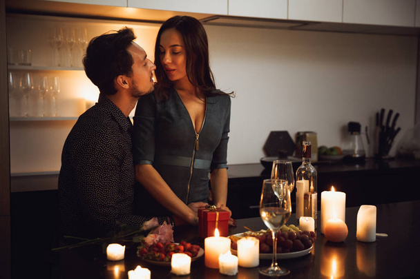 Beautiful passionate couple having a romantic candlelight dinner at home, kissing - Foto, Imagem