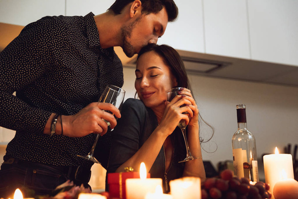 Beautiful passionate couple having a romantic candlelight dinner at home, kissing - Photo, Image