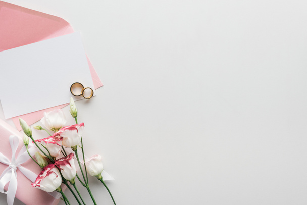 vista superior do cartão vazio com envelope rosa, flores, presente embrulhado e anéis de casamento dourados no fundo cinza
 - Foto, Imagem