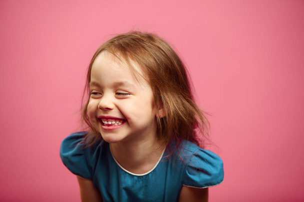 Portrait of child girl with a smile looking to the side on pink isolated background. - Фото, изображение