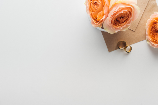 top view of brown envelope, flowers and golden wedding rings on grey background - Fotografie, Obrázek