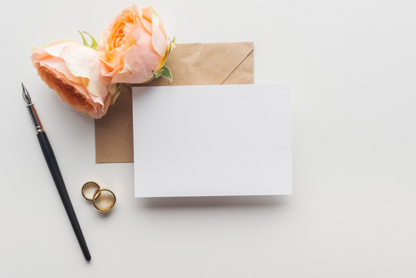 felülnézete a szürke háttér üres kártya barna kézműves papír boríték, toll, rózsa és Arany eljegyzési gyürük - Fotó, kép