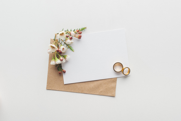 top view of empty card with brown craft paper envelope and wedding rings on grey background - Photo, Image