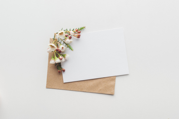 top view of empty blank with brown craft paper envelope and flowers on grey background - Fotó, kép