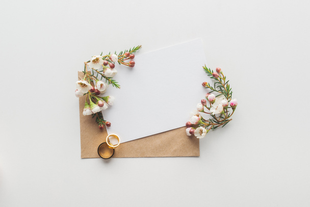 pohled shora na prázdnou kartu s hnědou obálku, květiny a snubní prsteny na šedém pozadí - Fotografie, Obrázek