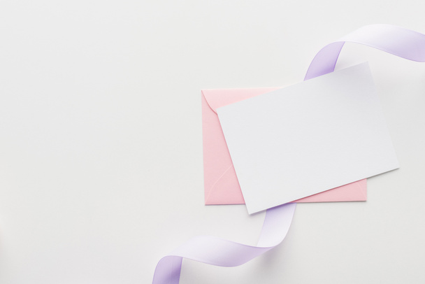 top view of empty blank with pink envelope and purple silk ribbon on grey background - Foto, imagen