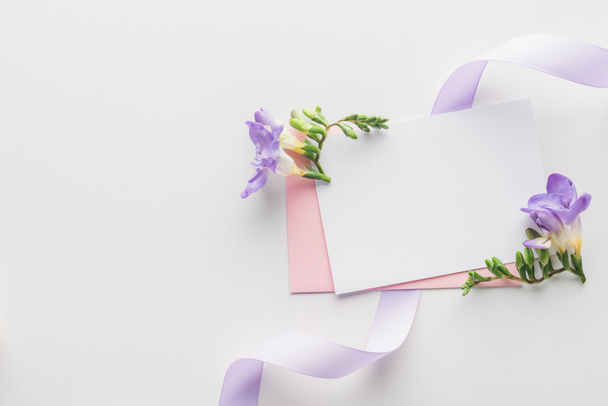 вид зверху порожня порожня з рожевим конвертом, фіолетовими квітами та шовковою стрічкою на сірому фоні
 - Фото, зображення