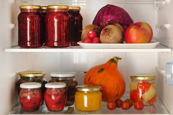 Pots avec confitures maison de fruits et de baies et légumes et fruits rouges, violets et orange frais sur étagère au réfrigérateur. Concept d'aliments végétariens sains fermentés
. - Photo, image