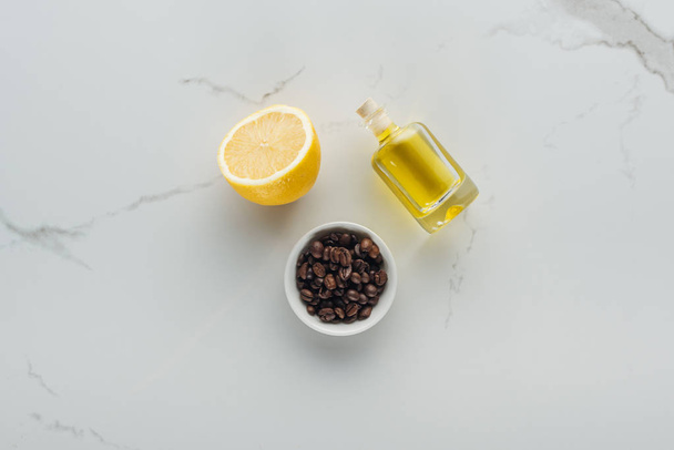 Draufsicht auf Schüssel mit Kaffeekörnern, halber Zitrone und einer Flasche Zitronensaft auf weißer Oberfläche - Foto, Bild