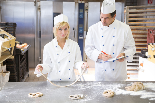 Baker instructs apprentice how to form pretzel - Foto, Imagen
