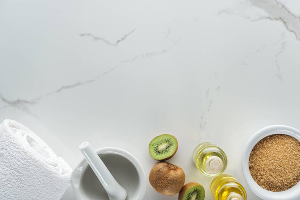 bovenaanzicht van Ponder, handdoek, kiwi en verschillende ingrediënten voor handgemaakte cosmetica op witte ondergrond - Foto, afbeelding